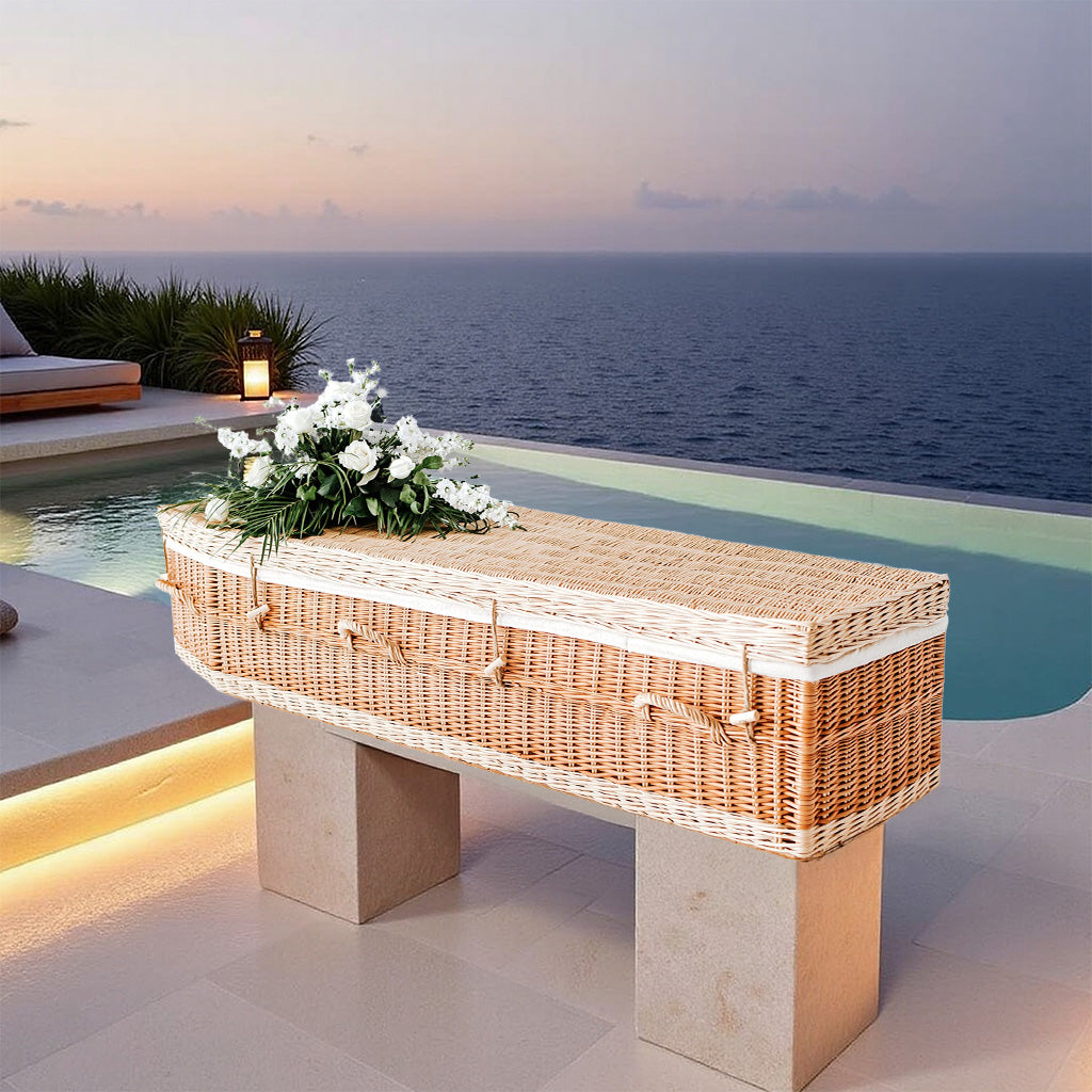 Handgevlochten wilgenteen uitvaartmand Warm Touch met ringgrepen, geplaatst op een verhoogd plateau aan een infinity pool, in de warme gloed van de avondzon met uitzicht over de kalme zee.